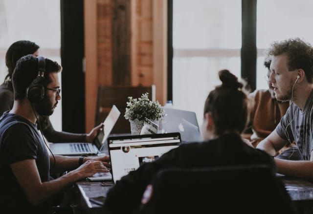 A diverse group of individuals sitting around a table, engrossed in their work on laptops.